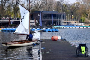 Anlegendes Segelboot und leerer Rollstuhl am Bootssteg. Aufgenommen bei inklusiver Regatta am Aasee.